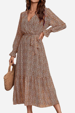 Woman wearing a floral Bloom Wrap Midi Dress with long sleeves and a waist tie holding a woven bag