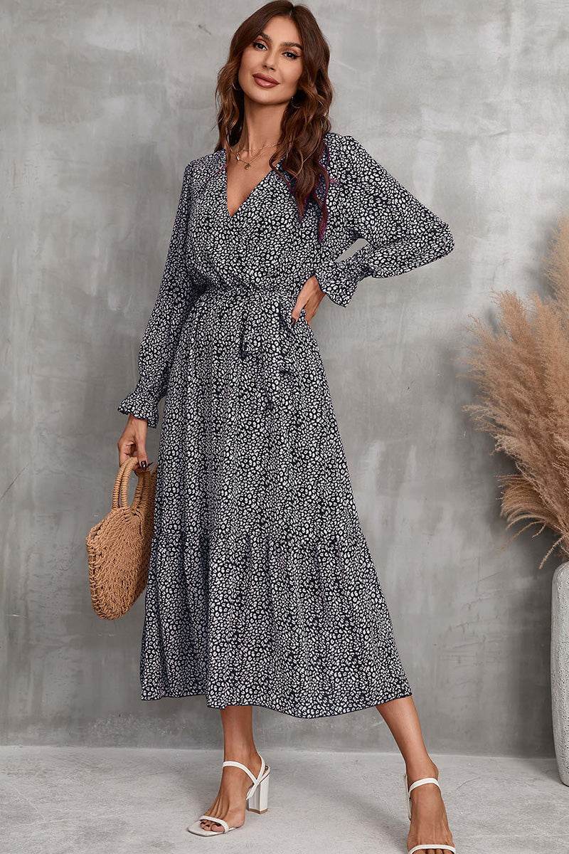 Woman wearing Bloom Wrap Midi Dress with floral print, long sleeves, and A-line silhouette, holding a woven handbag.