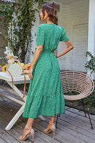 Back view of woman wearing a green charming floral boho maxi dress with short sleeves and ruffle hem standing on wooden patio