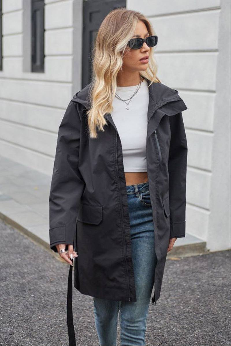 Woman wearing black water-resistant windbreaker trench jacket with belt and sunglasses outdoors