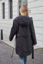 Woman wearing black water-resistant windbreaker trench jacket with hood and belt outdoors