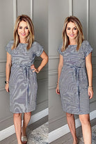 Woman wearing airy stripe sheath cotton dress with tie waist and short sleeves standing indoors