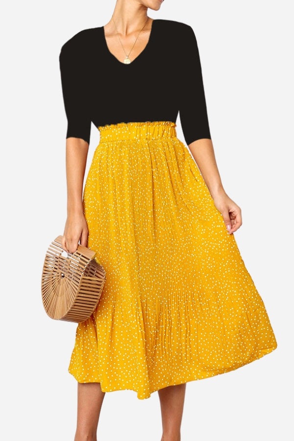 Woman wearing an effortlessly chic yellow polka dot pleated midi skirt with a high waist and black top carrying a wooden handbag.