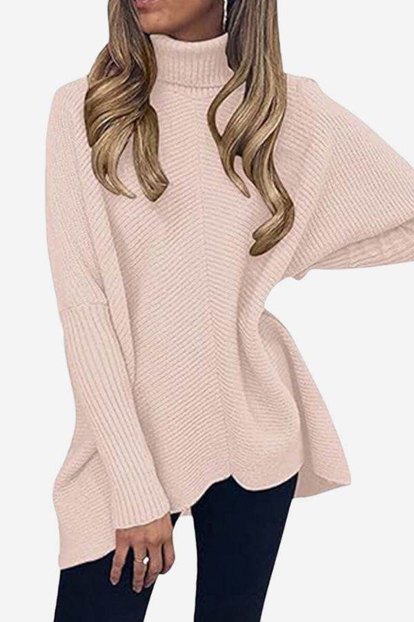 Woman wearing a blush pink cozy oversized knit pullover with long sleeves and turtleneck collar.