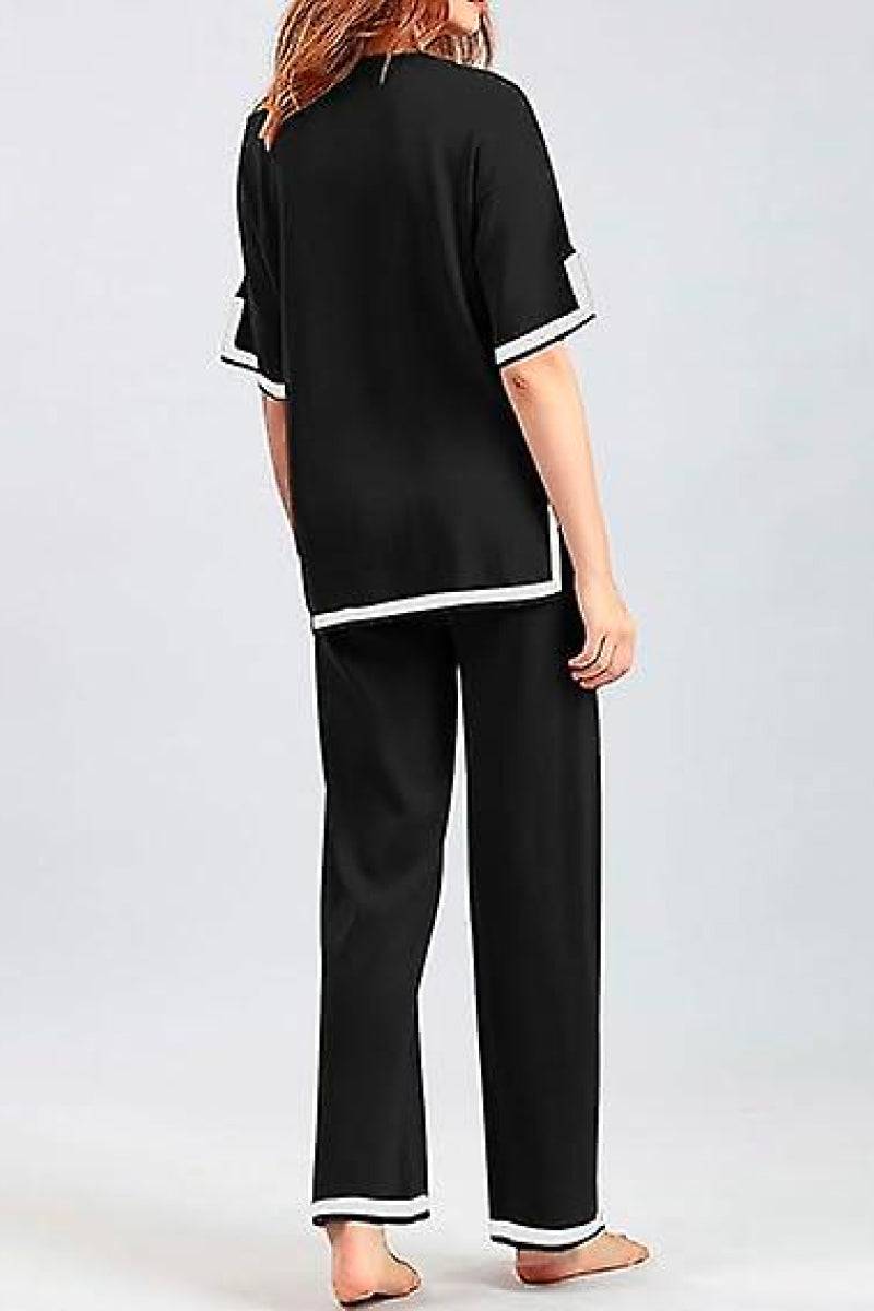 Back view of a woman wearing a black short sleeved relaxed fit lounge two-piece set with white trim on sleeves and pant cuffs