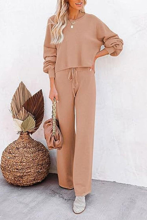 Woman wearing beige round neck loose fit cozy two-piece set with wide-leg pants and long sleeves, styled casually with a handbag and heeled shoes.