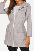 Woman wearing gray outdoor and travel hooded raincoat windbreaker jacket with zip front and pockets