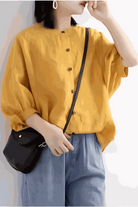 Relaxed loose breathable linen blouse in vibrant yellow with button-down front and puff sleeves, styled with casual blue pants and black shoulder bag.