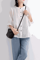 Woman wearing relaxed loose breathable white linen blouse with black buttons and blue jeans carrying a black purse