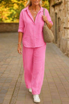 Woman wearing pink relaxed shirt and trousers two-piece set with rolled sleeves and white sneakers walking outdoors