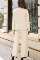 Woman wearing a long sleeved relaxed fit cream lounge two-piece set with black trim, standing outdoors with back facing camera