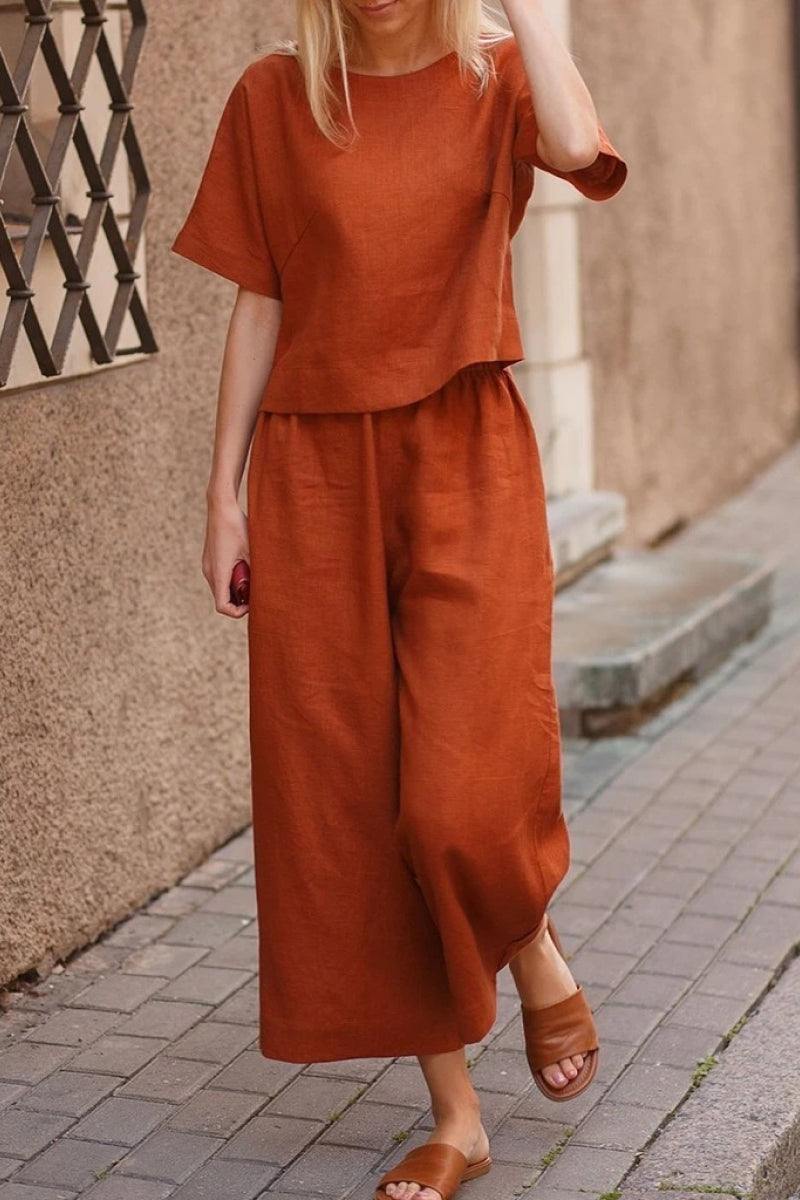 Woman wearing rust-colored loose fit co-ord set with short sleeves and wide-leg pants walking on a city sidewalk