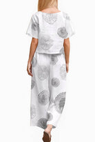 Back view of woman wearing white loose fit co-ord set with black circular floral prints, featuring a short-sleeve top and wide-leg pants.