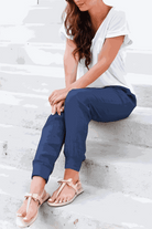 Woman wearing relaxed chic elastic ankles pants in navy blue sitting on stairs with white top and sandals