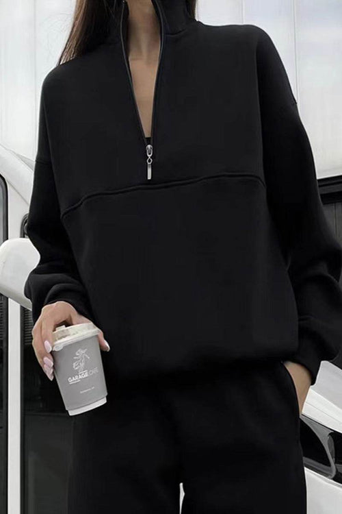 Woman wearing black cotton-blended two-piece tracksuit with high collar and zipper holding coffee cup