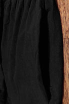 Black capped-sleeve voluminous pleated midi dress with airy sleeves and pockets on wood floor background