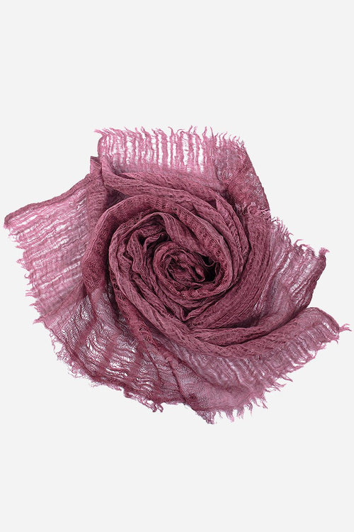 Lightweight linen scarf in soft mauve with frayed edges, rolled in a rose shape on white background