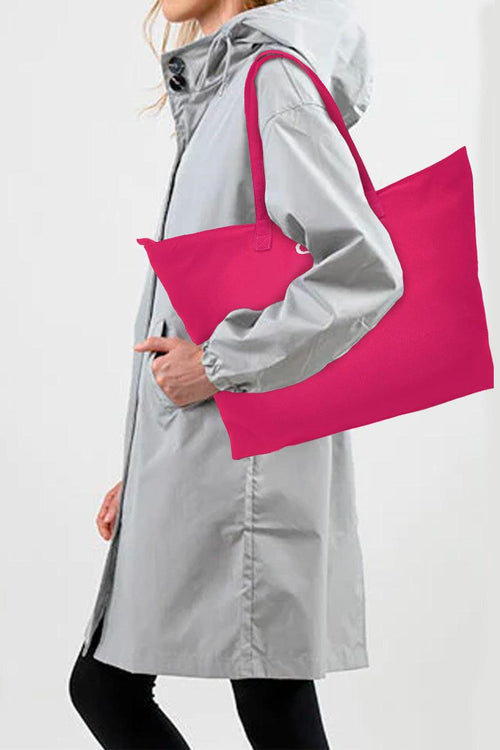 Woman in gray raincoat carrying large pink waterproof travel bag over shoulder