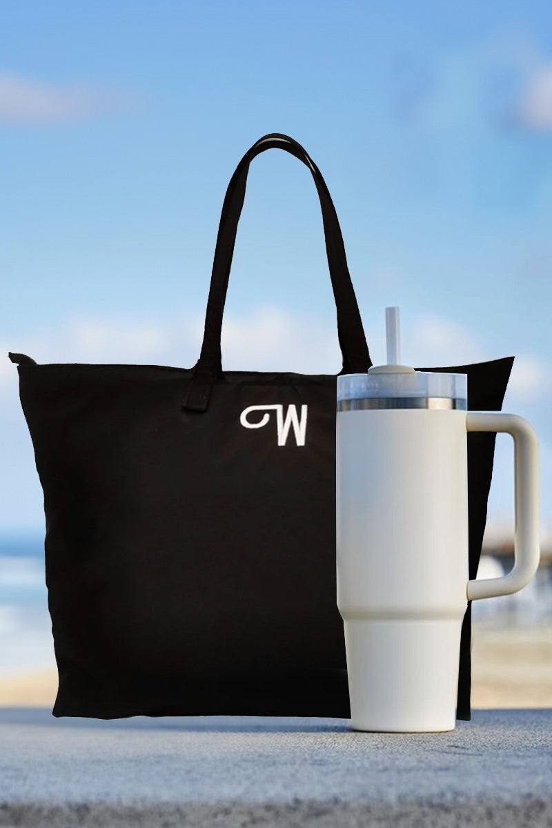 White indestructible travel cup with handle and straw next to black tote bag against blue sky background