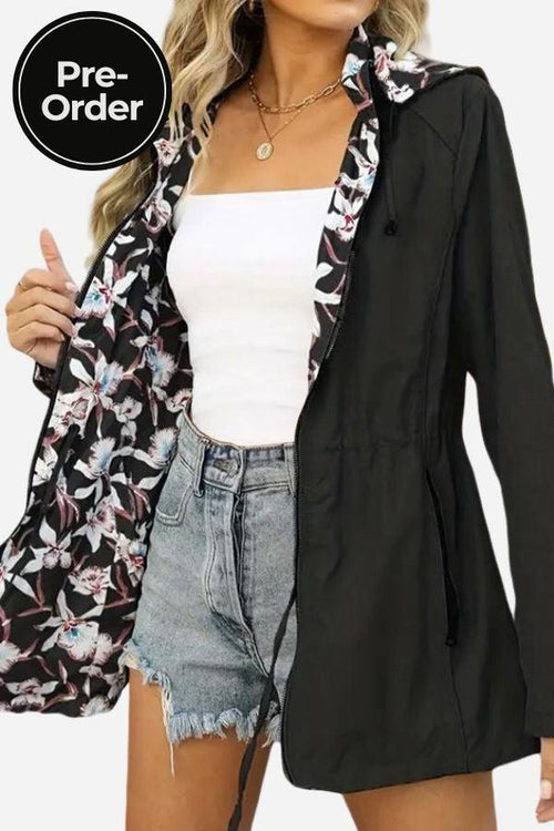 Woman wearing reversible floral raincoat with black exterior and floral print interior, paired with white top and denim shorts