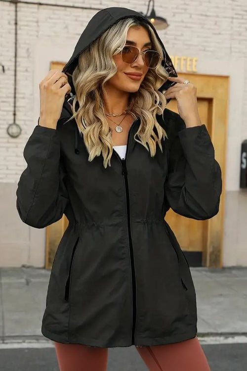 Woman wearing a black reversible floral raincoat with hood and zipper, styled for all-weather confidence and elegant fit
