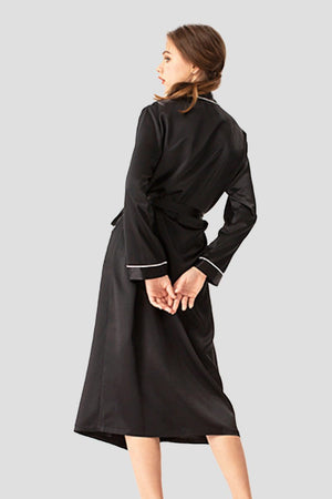 Woman wearing a black 100% mulberry silk belted classy nightgown with long sleeves and white trim on cuffs, viewed from the back.