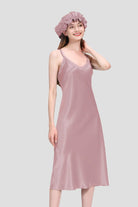 Woman wearing a light pink mulberry silk elegant night dress and matching cap against a plain background