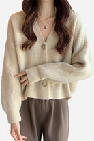 Woman wearing beige casual loose boxy cardigan with V-neck and buttons paired with brown pants