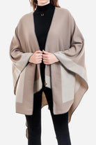 One size elegant knitted poncho in two-tone beige and taupe colors with flowing silhouette worn over black outfit