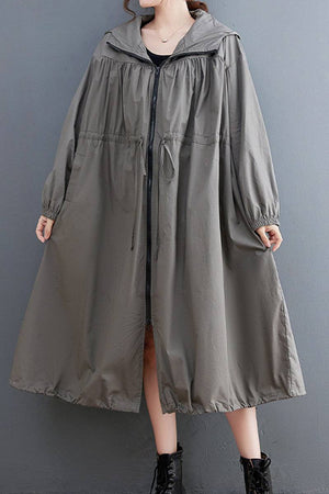 Oversized all-weather water-resistant windbreaker in neutral color with drawstring waist and elastic cuffs, styled with ankle boots