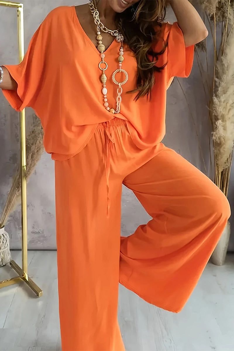 Woman wearing vibrant orange two-piece pantsuit with loose fit and statement necklace