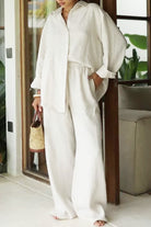 woman wearing white 100% cotton Wanderlust two piece set with long sleeves and wide pants indoors carrying woven bag