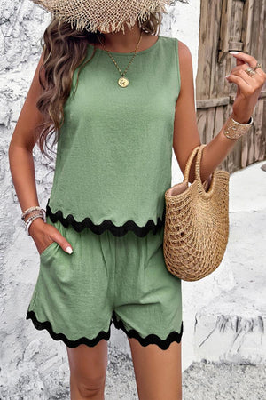 Woman wearing green flattering coastal scallop two-piece set with scalloped black trim, straw hat, and woven bag outdoors