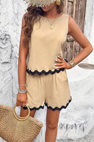 Woman wearing flattering coastal scallop two-piece beige set with black scalloped edges, styled with straw hat and woven bag.
