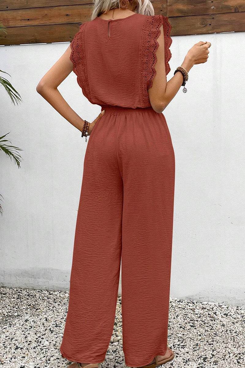 Woman wearing rust-colored elegant two-piece set with lace details on top and wide-leg pants, standing outdoors.