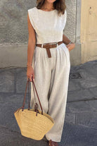 Woman wearing cotton-linen blend sleeveless crop top and wide-leg pants summer outfit with brown belt and straw handbag