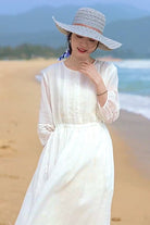 Woman wearing a white 100% linen coastal shift dress with long sleeves and lace details on a beach.