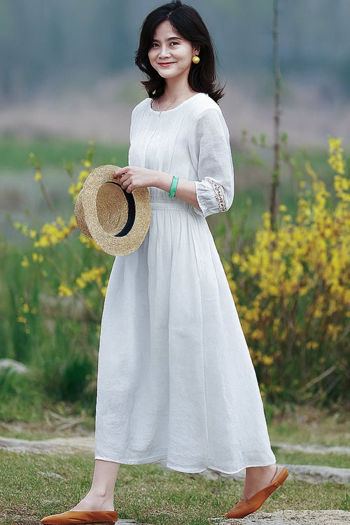 Woman wearing a white 100% linen coastal shift dress holding a straw hat outdoors.