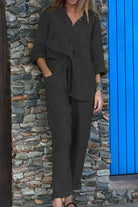 Woman wearing a black Casual Chic Two-Piece Set with a relaxed fit, long sleeves, and drawstring pants next to a stone wall and blue door.