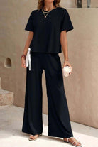 Woman wearing Riviera Relaxed Two Piece Set black wide-leg pants and loose short-sleeve top, casual elegant travel outfit