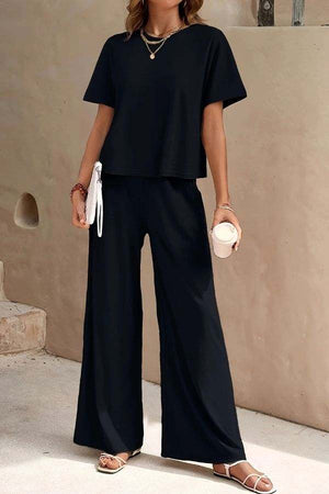 Woman wearing Riviera Relaxed Two Piece Set black wide-leg pants and loose short-sleeve top, casual elegant travel outfit