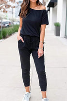 Woman wearing black Moonlit Rome Off-Shoulder jumpsuit with pockets and tapered legs outdoors