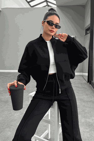 Woman wearing The Voyager Zip Set black zip-front sweatshirt and wide-leg joggers holding a drink cup, styled for travel and casual wear