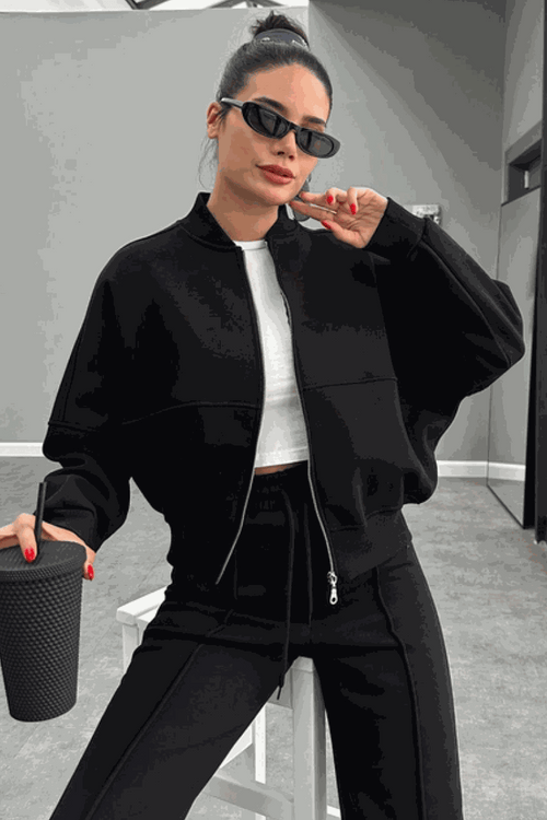 Woman wearing The Voyager Zip Set black zip-front sweatshirt and wide-leg joggers holding a cup, styled for travel and casual comfort.