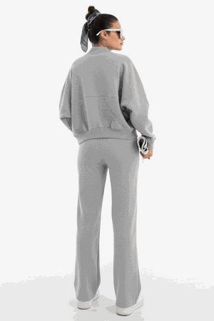 Woman wearing The Voyager Zip Set in light gray, featuring a relaxed zip-front sweatshirt and wide-leg joggers with pockets, styled for comfort and travel.