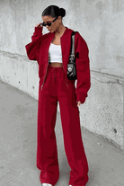 Woman wearing The Voyager Zip Set in red, featuring a relaxed zip-front sweatshirt and wide-leg joggers with pockets.