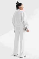 Woman wearing white Voyager Zip Set with zip-front sweatshirt and wide-leg joggers, styled with sunglasses and hair scarf, standing against white background