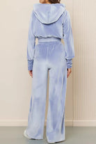 Back view of woman wearing light blue velour tracksuit with cropped hoodie and high-waist pants