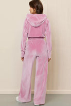 Woman wearing pink velour tracksuit with cropped hoodie and high-waist pants from the back