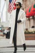 Woman wearing white oversized teddy coat with longline silhouette and black accessories on city street